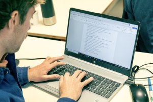 Une personne vue de dos tape écrit sur un ordinateur portable vu de face