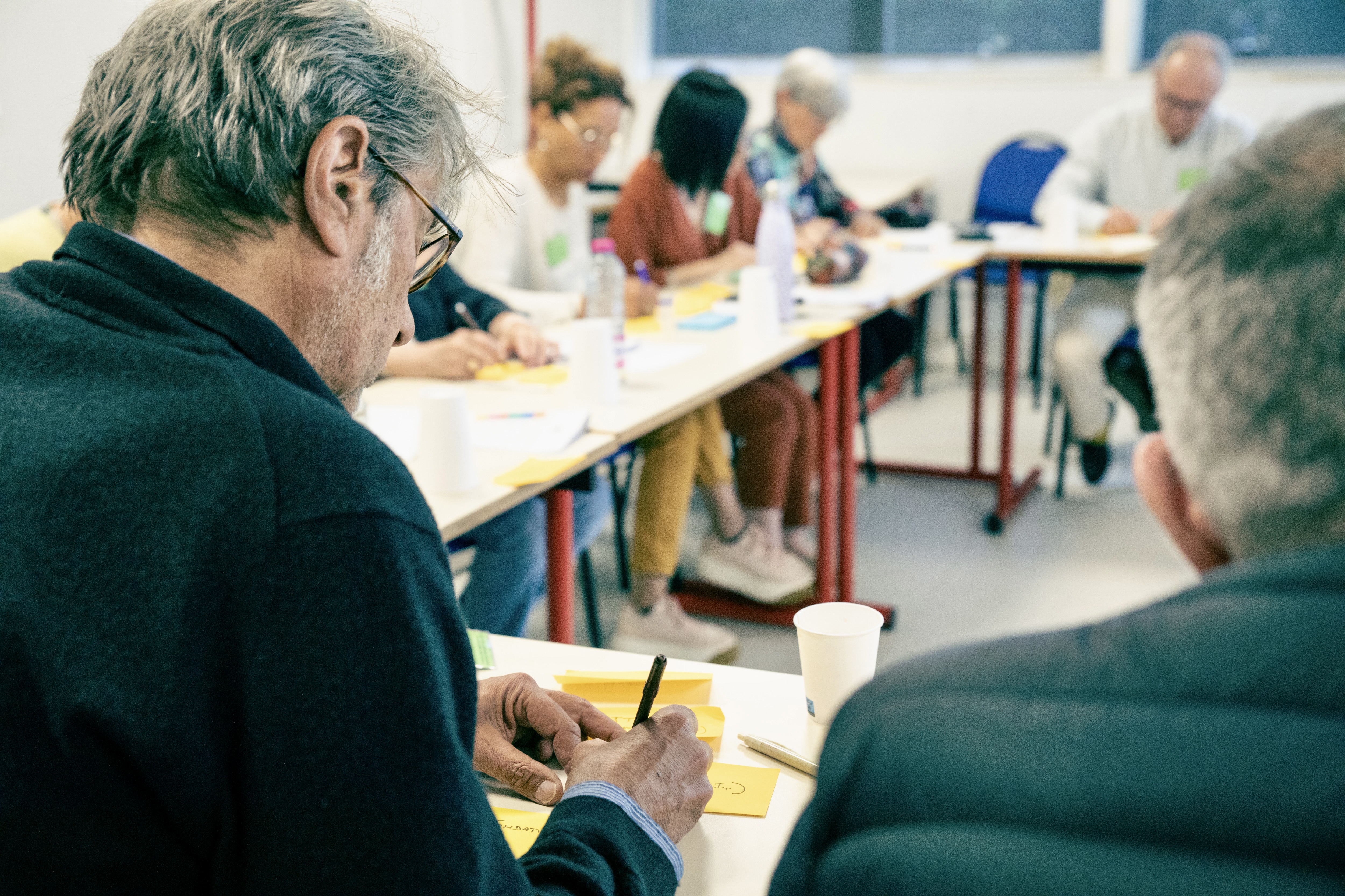 Des participants assis à des tables en train d'écrire sur des petits papiers